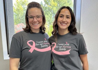 two people smiling, wearing breast cancer shirts