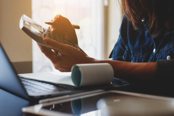 close up of person doing payroll and using a calculator and laptop