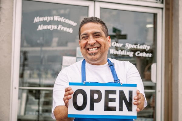 man smiling, holding open sign in front of business