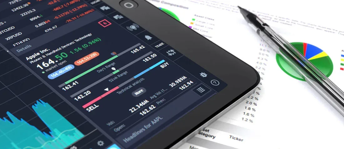 A tablet displaying stock market data with graphs and buy/sell options on a table. Beside it, printed sheets showcase colorful pie charts and a pen resting nearby.